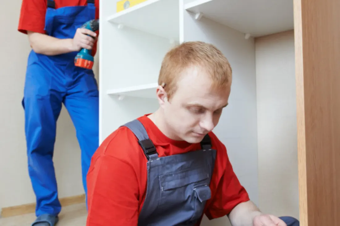 Monter siedzi przy szafie i czyta rysunek projektu, a drugi z wkrętarką stoi przy białych półkach