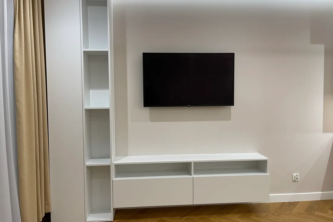 Biała zabudowa RTV w salonie: wysoka szafa z otwartym regałem i wisząca szafka z dwiema szufladami pod telewizorem