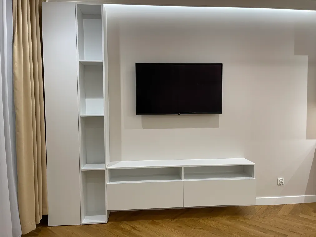 Biała zabudowa RTV w salonie: wysoka szafa z otwartym regałem i wisząca szafka z dwiema szufladami pod telewizorem